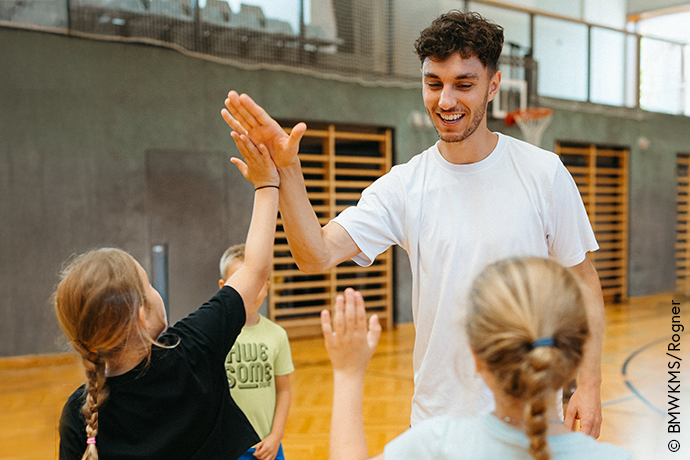 Symbolbild Ehrenamtspreis, Trainer mit Kindern in der Sporthalle, High Five