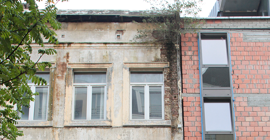 Leerstehendes Haus, Pflanzen wachsen aus den kaputten Verputz und daneben ein Neubau